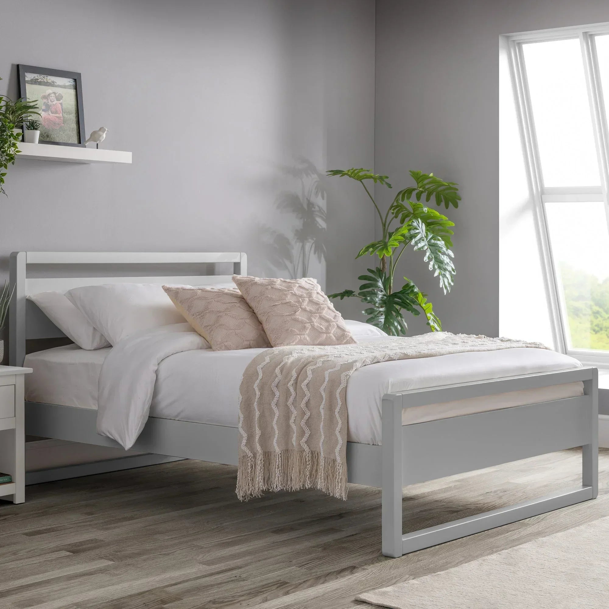 Dove grey bed frame with white bedding and beige throw in modern bedroom with window light