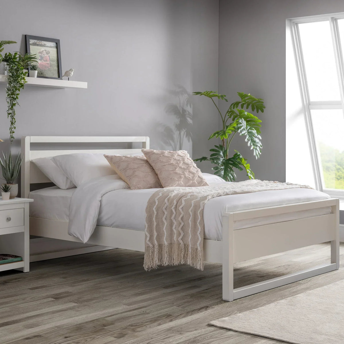 White wooden bed frame with white bedding, beige cushions, and throw in modern bedroom