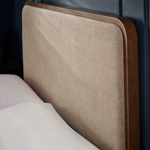 Close-up side view of beige upholstered headboard and dark wood frame edge with white bedding