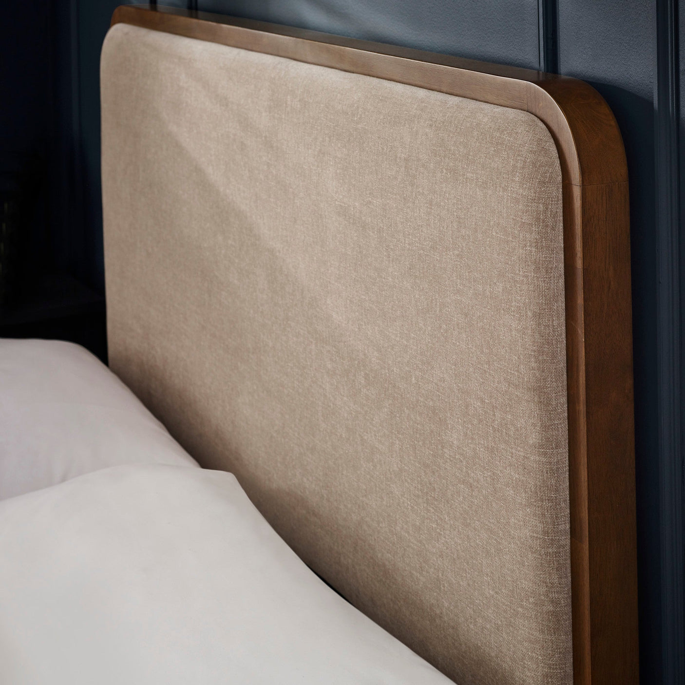 Close-up side view of beige upholstered headboard and dark wood frame edge with white bedding