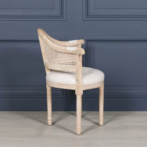 Light wood dining chair with curved cane back and cream upholstered seat, side view