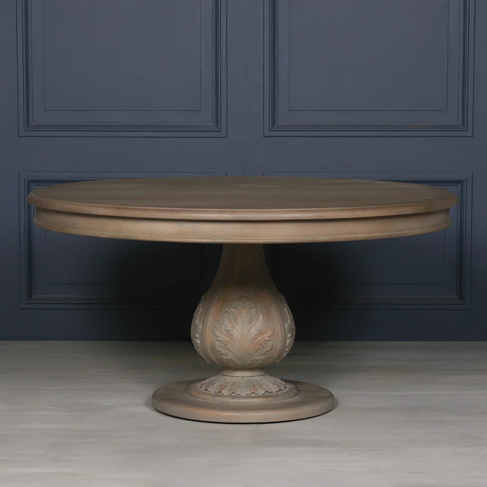 Round wooden dining table with carved pedestal base against dark paneled wall
