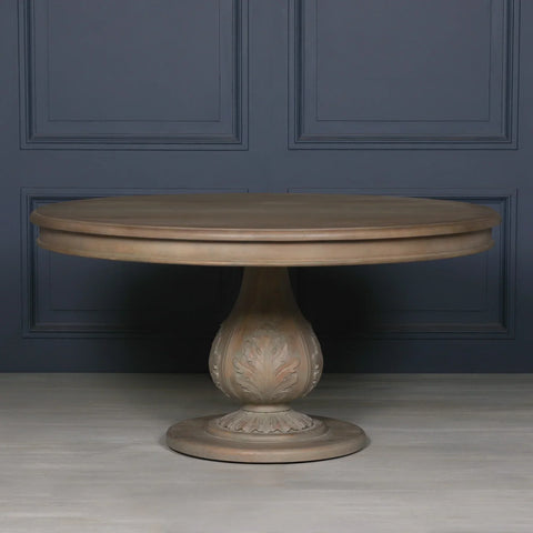 Round wooden dining table with carved pedestal base against dark paneled wall