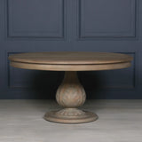 Round wooden dining table with carved pedestal base against dark paneled wall