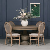 Round oak dining table with carved pedestal base and four rattan back chairs, floral centerpiece