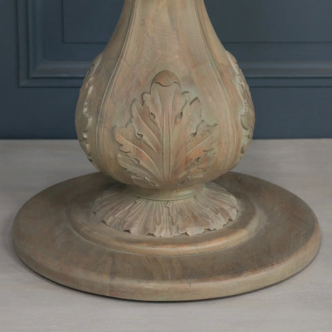 Carved wood dining table pedestal base with leaf detailing on light wood floor