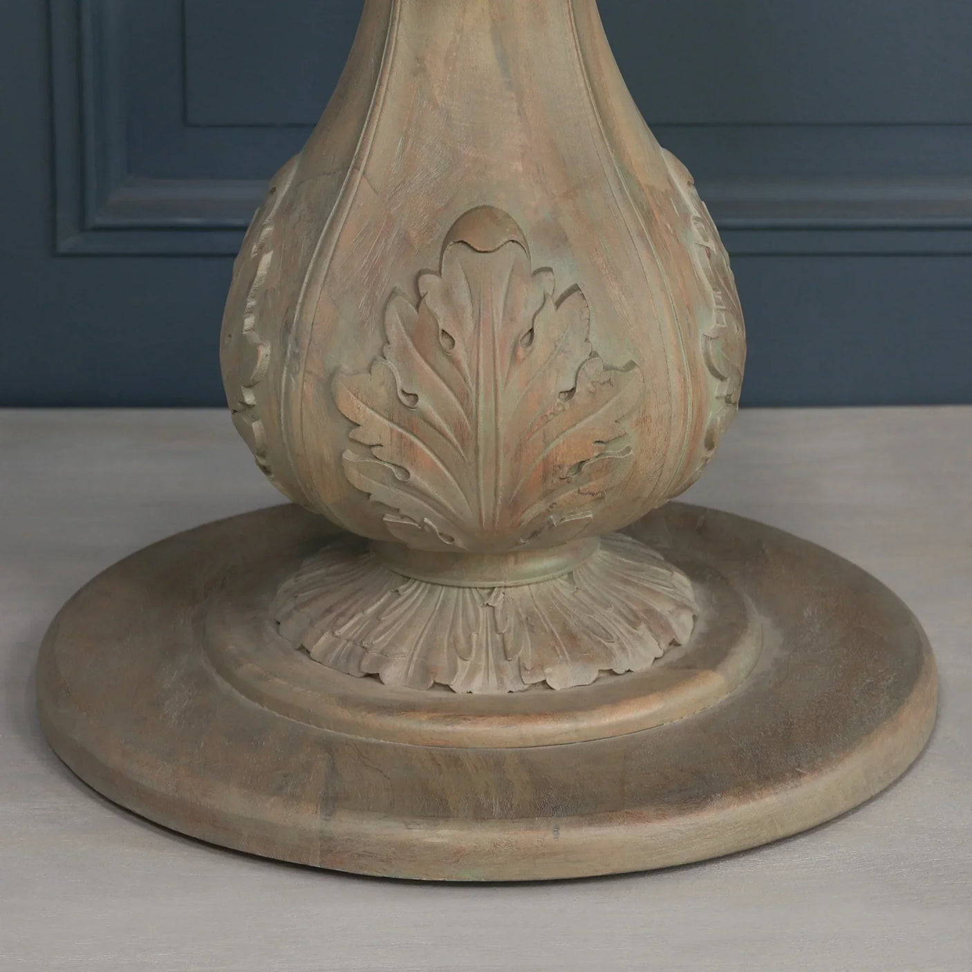 Carved wood dining table pedestal base with leaf detailing on light wood floor