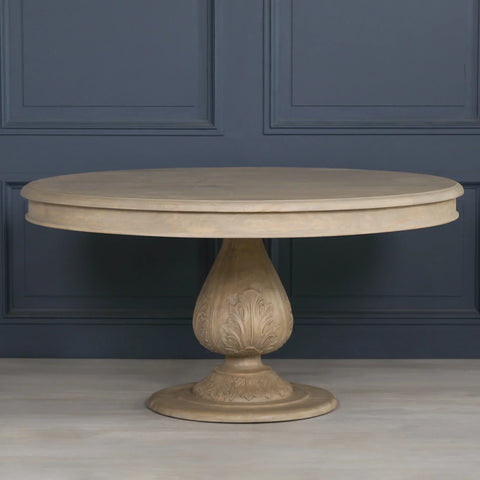 Round wooden dining table with carved pedestal base against blue paneled wall