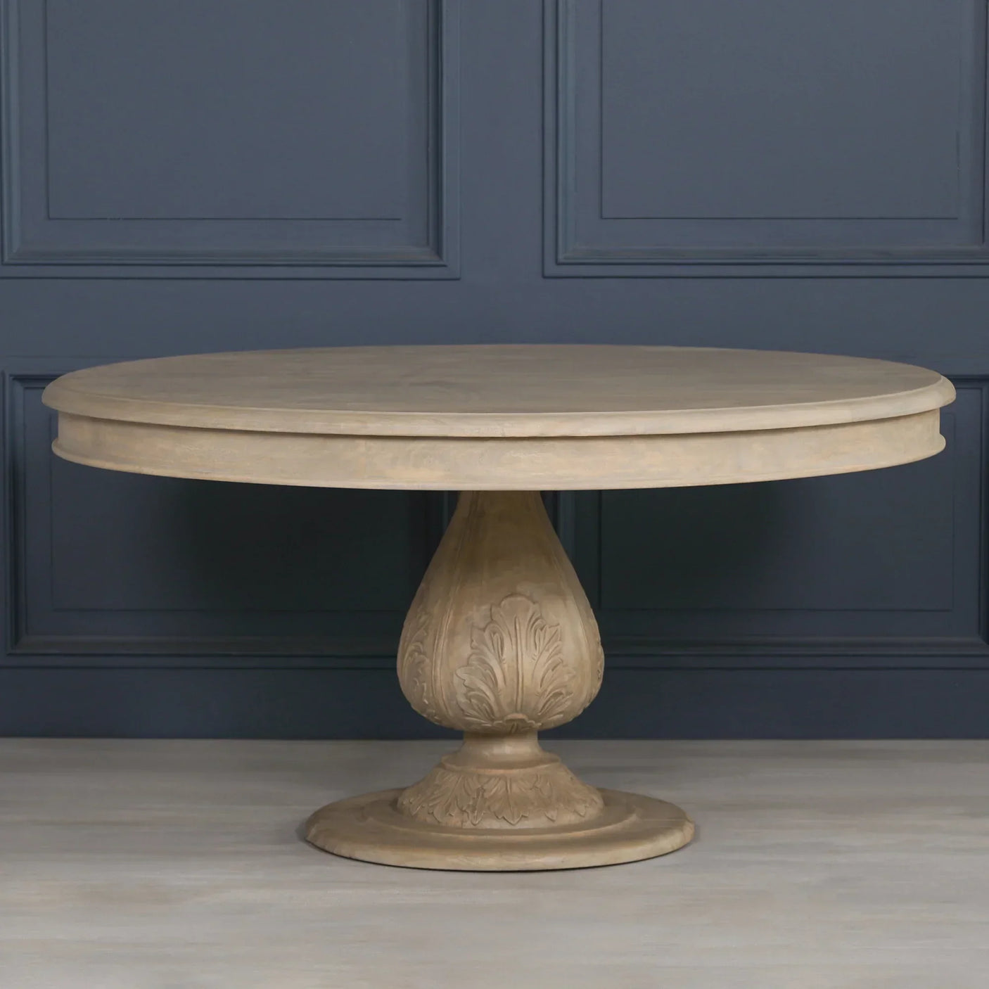 Round wooden dining table with carved pedestal base against blue paneled wall