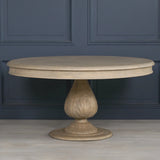 Round wooden dining table with carved pedestal base against blue paneled wall