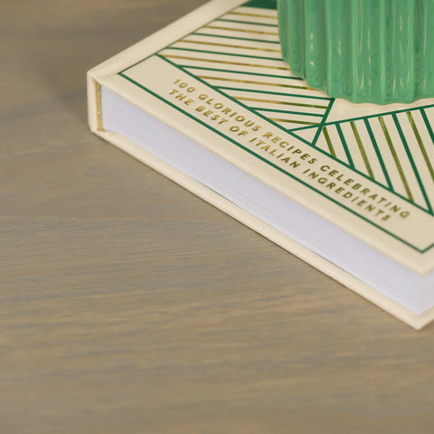 Light wood table surface closeup with book and green ceramic decor accent on top