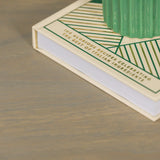 Light wood table surface closeup with book and green ceramic decor accent on top