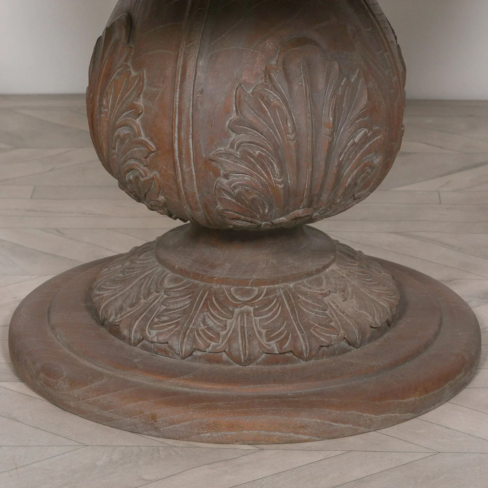 Carved wood pedestal table base with leaf pattern detail on light herringbone floor