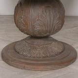 Carved wood pedestal table base with leaf pattern detail on light herringbone floor