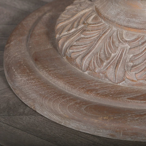 Rustic wooden dining table base with carved leaf detail on dark wood flooring