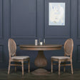Round wooden dining table with pedestal base and two cane back dining chairs in classic room