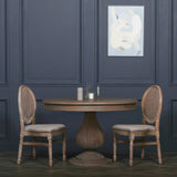 Round wooden dining table with pedestal base and two cane back dining chairs in classic room