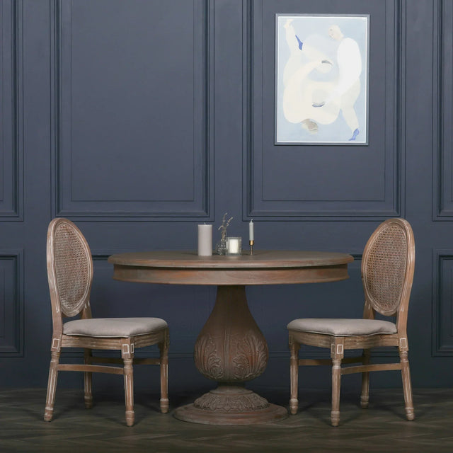 Round wooden dining table with pedestal base and two cane back dining chairs in classic room
