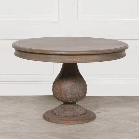 Round wooden dining table with carved pedestal base on light floor