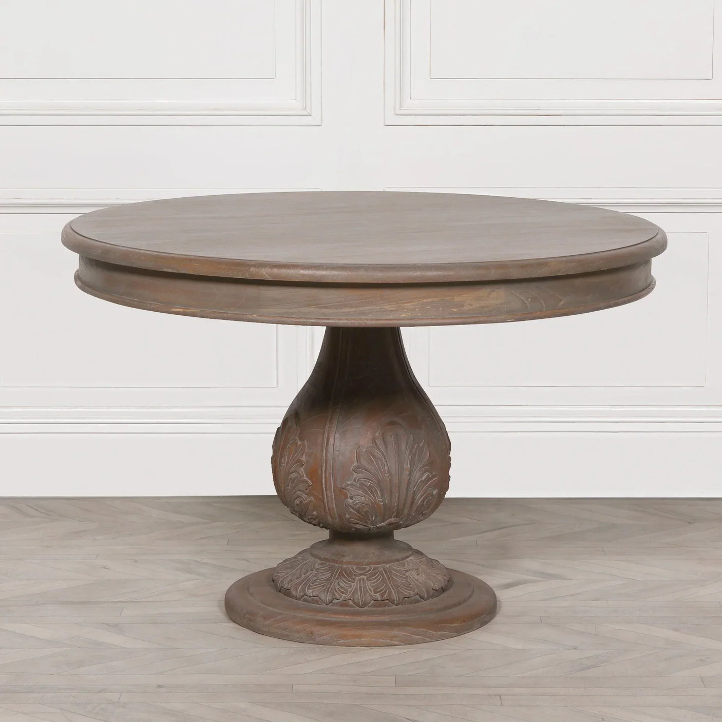 Round wooden dining table with carved pedestal base on light floor