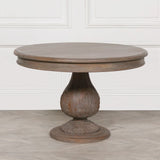 Round wooden dining table with carved pedestal base on light floor