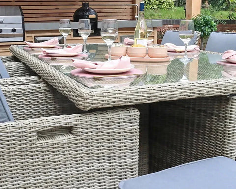 Rattan outdoor dining set with glass top table, cushioned seats, and tableware arranged
