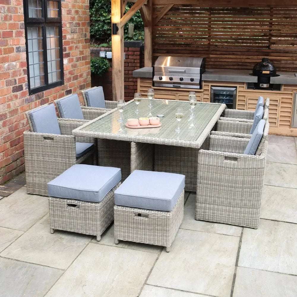 Rattan garden dining set with glass top table and grey cushions on a patio near outdoor kitchen