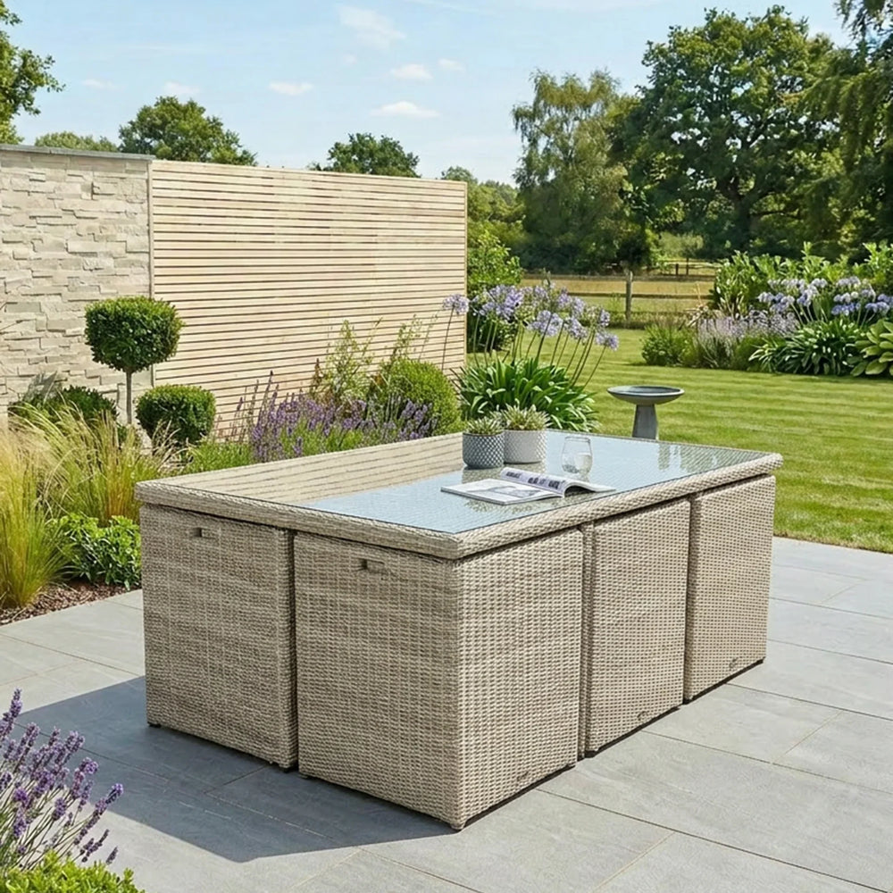 Beige rattan outdoor dining set with glass-top table and stools on patio in garden