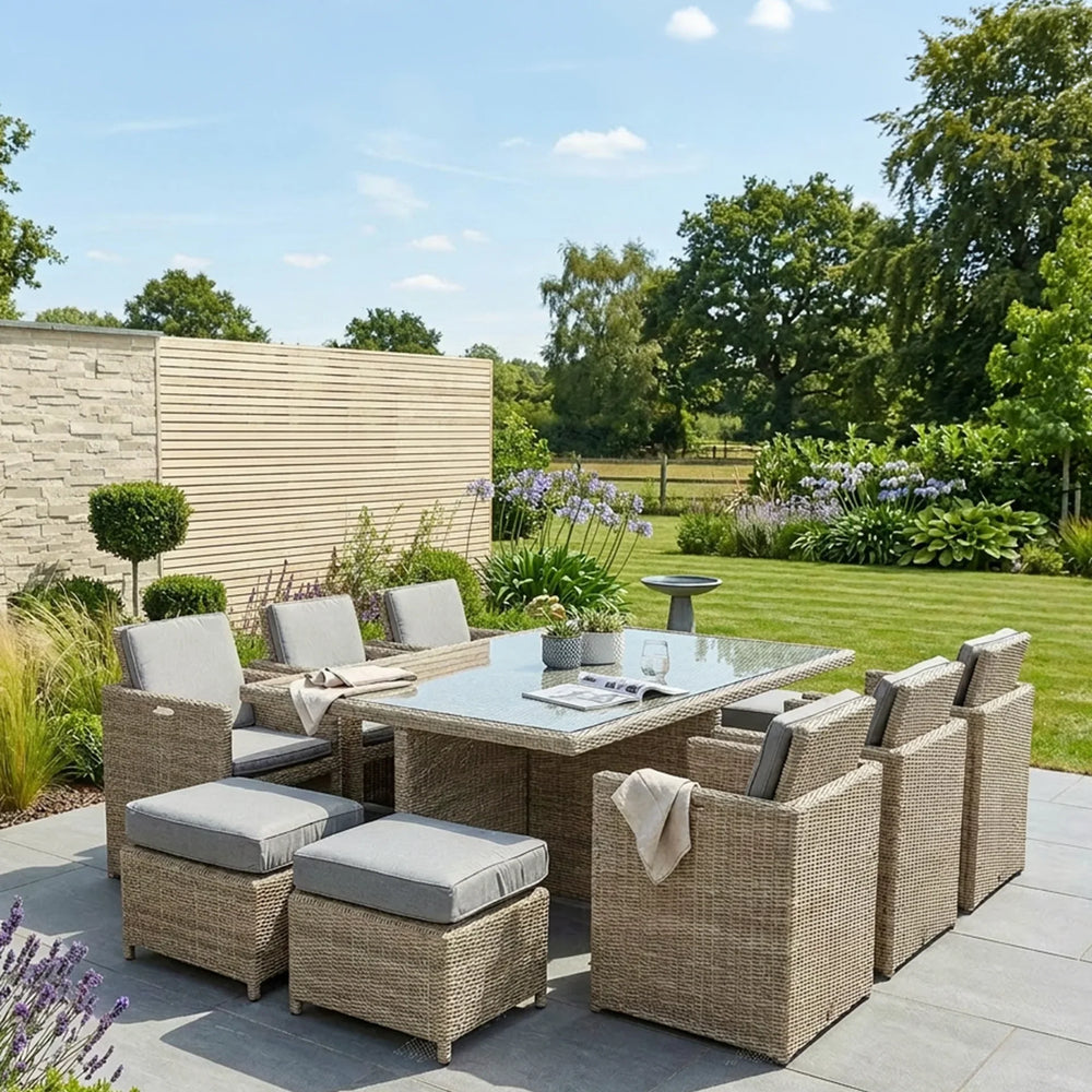 Rattan outdoor dining set with glass table, cushioned chairs and stools on a patio garden