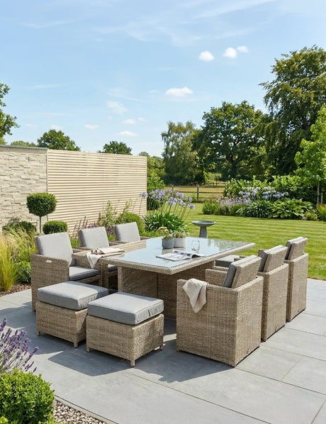 Rattan outdoor dining set with glass table, cushioned chairs and stools on a patio garden