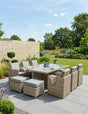 Rattan outdoor dining set with glass table, cushioned chairs and stools on a patio garden