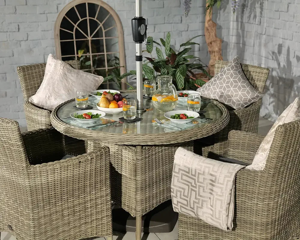 Round rattan garden dining set with four cushioned chairs and glass top table fully set
