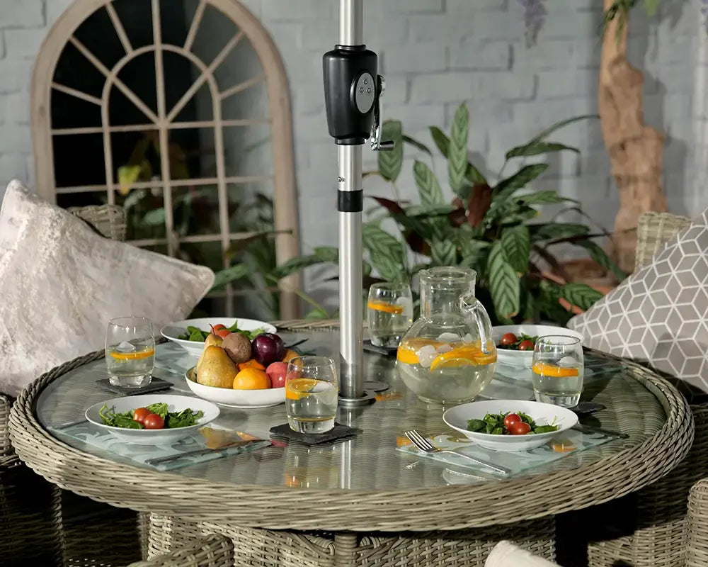 Rattan outdoor dining table with glass top set for four, jug of water and fruit bowl