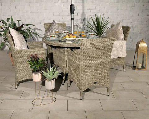 Rattan garden dining set with glass table, four wicker chairs, cushions, and tableware
