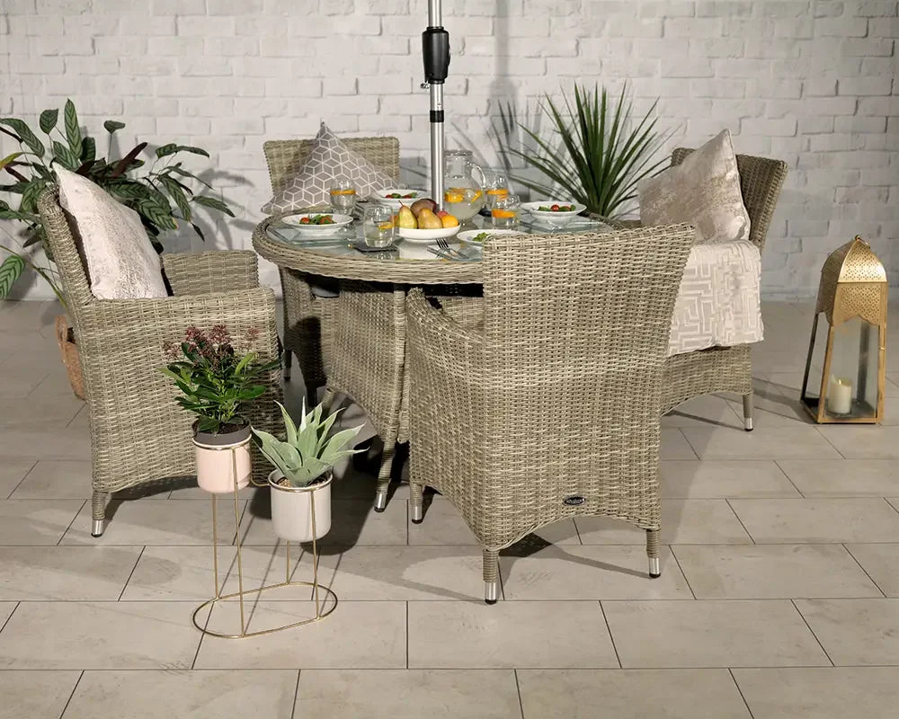 Rattan garden dining set with glass table, four wicker chairs, cushions, and tableware