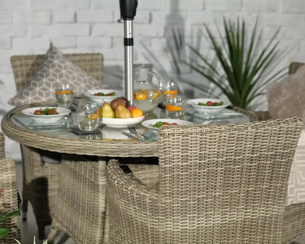Round rattan dining table set with glass top and four wicker chairs, outdoor setting
