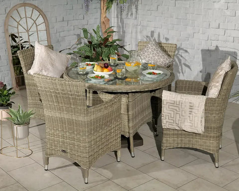Round rattan garden dining set with glass table, four cushioned chairs, and tableware