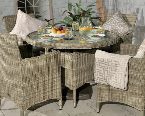 Round rattan garden dining set with glass table, four chairs, and tableware setup