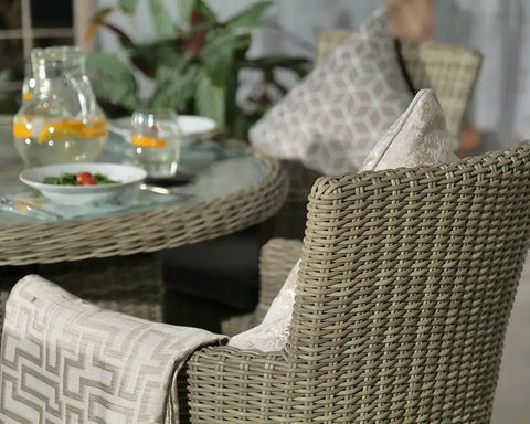 Round rattan dining table with glass top and matching woven armchairs set for a meal