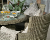 Round rattan dining table with glass top and matching woven armchairs set for a meal