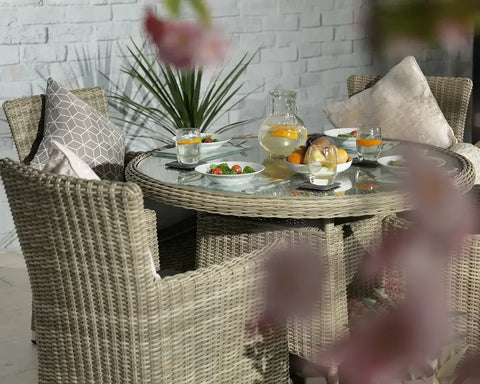 Round rattan garden dining set with glass top table and cushioned chairs arranged for lunch