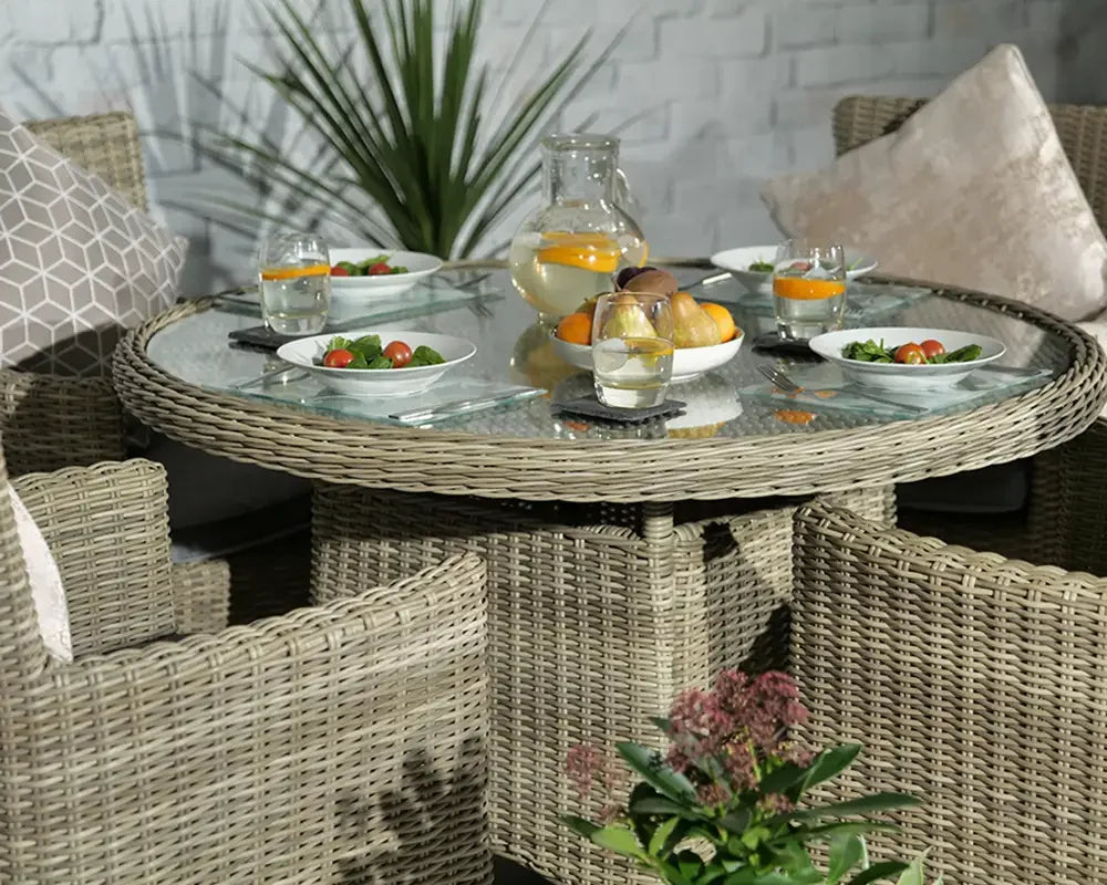 Round rattan dining set with glass top, four chairs, and plates of salad on outdoor patio