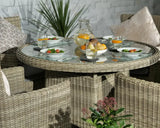 Round rattan dining set with glass top, four chairs, and plates of salad on outdoor patio