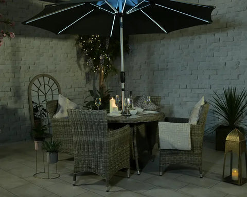 Rattan garden dining set with four armchairs, round table, LED parasol and cushions at dusk