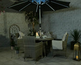 Rattan garden dining set with four armchairs, round table, LED parasol and cushions at dusk