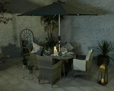 Rattan garden dining set with four chairs, round table, and parasol on tiled patio at night