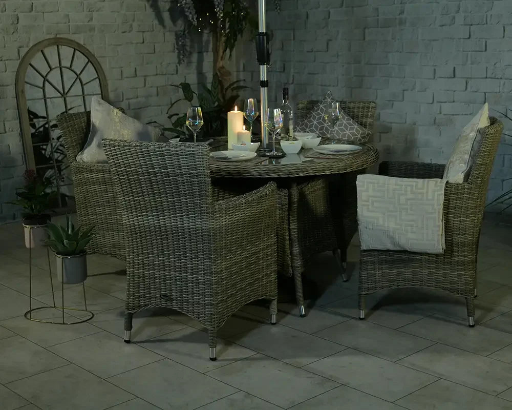 Rattan garden dining set with four armchairs, round table, candles and glassware on patio