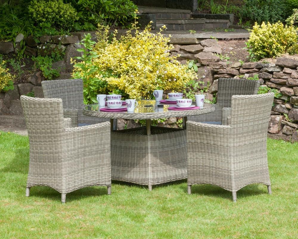Grey rattan garden dining set with four armchairs and glass-top table on grass