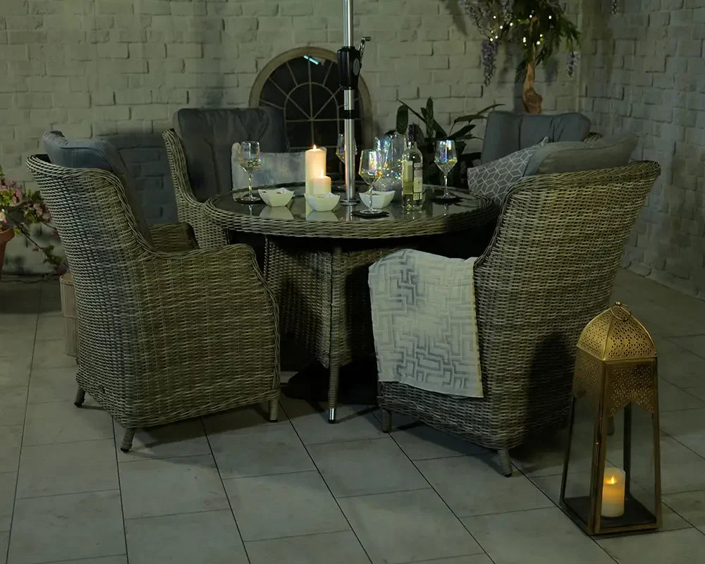 Grey rattan garden dining set with round table, armchairs, and cushions in evening setting