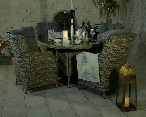 Grey rattan garden dining set with round table, armchairs, and cushions in evening setting